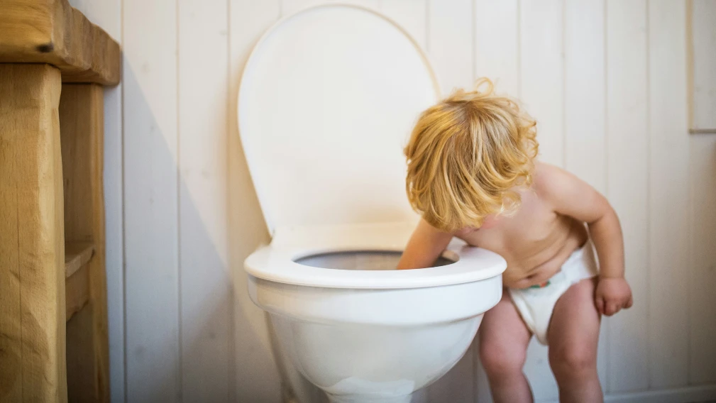 Cute toddler in the bathroom. Little boy putting his hand in the toilet.