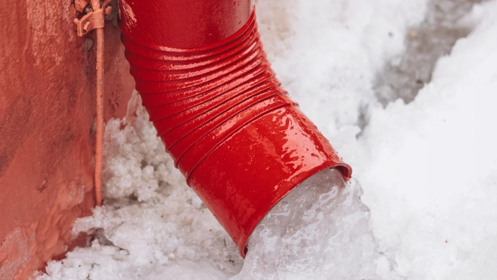 Red drainpipe with melting snow
